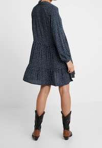 Vestito navy con motivi a foglia bianchi, orlo arricciato, maniche lunghe e una vestibilità rilassata. Abbinato a stivali cowboy neri e marroni.