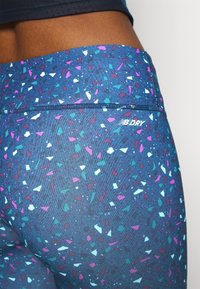 Leggings blu con motivo a macchie che presentano tonalità di rosa, teal e bianco. Include un piccolo logo "NB DRY" sulla vita.