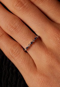 Saphir- und Diamantring aus Silber. Enthält abwechselnd birnenförmige Saphire und runde Diamanten, eingefasst in einem dünnen, polierten Band.