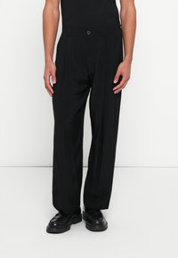 Μαύρο πλισέ παντελόνι με σχεδιασμό ίσιας γραμμής, ραμμένο σύμφωνα με το σώμα και κλείσιμο με κουμπί. Κατασκευα�σμένο από ελαφρύ υλικό, συνδυάζεται με μαύρα παπούτσια.