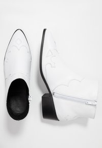 Botas de cuero blancas hasta el tobillo con punteras puntiagudas, costuras decorativas, cremallera lateral y tacones cuadrados negros, mostradas en vistas superior y lateral.