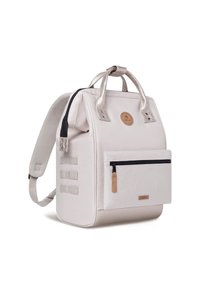 Sac à dos beige avec poignées métalliques argentées, une poche avant zippée, tissu texturé et un patch logo rond. Comprend des bretelles ajustables.