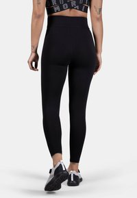 Black high-waisted leggings with a smooth texture and a fitted design, paired with white and grey athletic shoes.