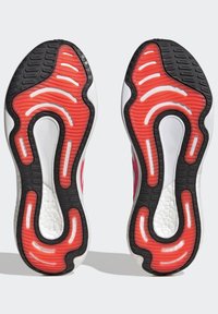 Suela de zapato con una suela exterior de goma negra y acentos rojos. Presenta patrones ondulados y áreas de agarre texturizadas para una mejor tracción.