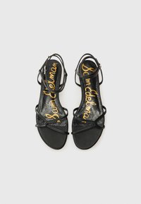 Mustad musta rihmadega sandaalid, millel on peened rihmad ja lame tall. Tekstuuriga must sisetald, millel on kuldsete tähtedega "Sam Edelman".
