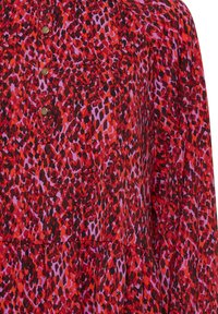 Abito stampato rosso e viola con un design fluido, scollatura rotonda e bottoni in ottone per la chiusura, caratterizzato da un aspetto testurizzato e stratificato.