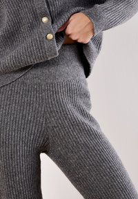 Maglione a coste grigio e pantaloni abbinati, con accenti in oro sui bottoni del maglione. Texture morbida e vestibilità comoda evidenti.