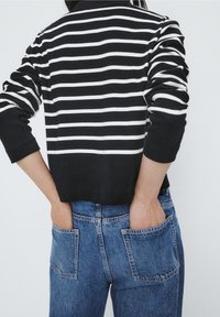 Czarny i biały sweter w paski o luźnym kroju, z długimi rękawami i krótkim fasonem, zestawiony z niebieskimi dżinsami z wysokim stanem.