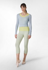 Lichtblauw langemouwen bovenkant met een textuurstof, gelaagd over een limoengroene tanktop, gecombineerd met pastelgroene leggings en naakte ballerina's.