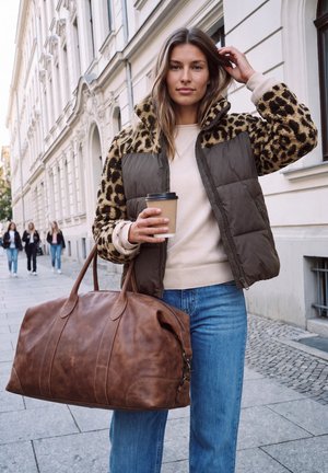 Femme portant une veste à imprimé léopard, tenant une tasse de café et un grand sac en cuir marron, debout sur un trottoir urbain avec des bâtiments historiques.