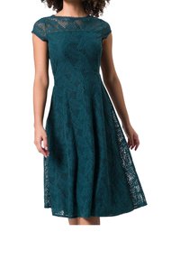 Robe en dentelle turquoise avec des manches courtes à bretelles, dotée d'un corsage ajusté et s'évasant en une jupe plus ample. Motifs de feuilles élaborés sur le tissu.