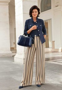 Marineblauwe cropped jas, zwarte top, beige gestreepte wijde broek, marineblauwe hakken en een gestructureerde marineblauwe tas met dubbele handvatten.