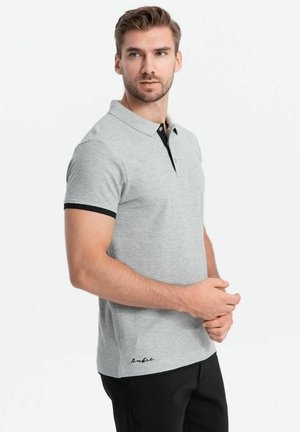 Grå polo shirt med sort krave og manchetter, korte ærmer og et subtilt logo broderet nederst. Stoffet ser glat og afslappet ud.