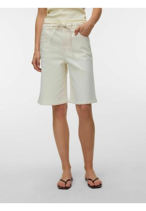 Kvinde iført off-white knælange shorts med snøre i taljen og slip-on sandaler, stående mod en ensfarvet hvid baggrund.