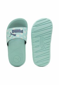 Šviesiai mėlynos šlepetės su gėlėmis, turinčios plačią juostą ir tekstūruotą padas. PUMA logotipas aiškiai matomas ant juostos.