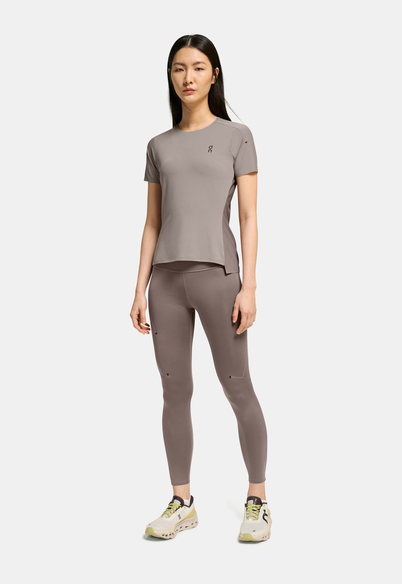Ljust brunt atletisk t-shirt och leggings, båda med en mjuk textur. T-shirten har rund hals och sidoflikar; leggingsen har subtila detaljer.