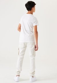 Witte katoenen t-shirt en lichtbeige cargobroek met zijritsen, elastische boorden en witte sneakers. Eenvoudig ontwerp met een ontspannen pasvorm.