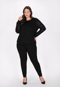 Top nero con maniche decorate da paillettes, abbinato a pantaloni neri aderenti e tacchi neri. Tessuto morbido, design casual con maniche lunghe.
