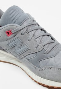 Grijze sneaker van suède en mesh materialen, met een opvallend grijs "N"-logo, roze accenten, platte veters en een gestructureerde rubberen zool.