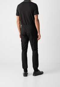 Schwarzes Poloshirt mit weißen Akzenten, kombiniert mit schwarzen Cargo-Hosen mit elastischem Bund und seitlichen Taschen. Getragen mit schwarzen Schuhen.