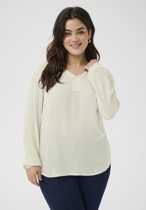 Blouse à manches longues et col en v de couleur crème clair avec une texture subtile. Dotée d'une patte de boutonnage à moitié, d'une coupe décontractée et d'un ourlet arrondi.