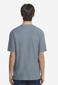 Grå kortärmad t-shirt med rund halsringning, med en texturerad tyg och en avslappnad passform. Inga synliga grafiska element eller mönster.