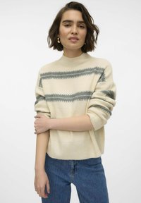 Maglione crema con righe orizzontali grigie, collo e polsini a coste. Abbinato a jeans blu a vita alta, che mostrano una vestibilità rilassata.