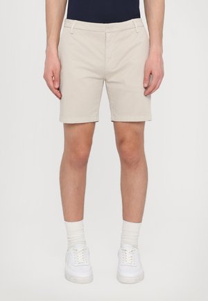Beige bomulds shorts med lige snit, forlommer og bæltestropper, kombineret med hvide sneakers og hvide sokker.