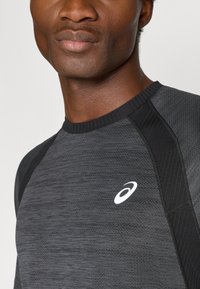 Μαύρο και γκρι αθλητικό μπλουζάκι με μακριά μανίκια, υφή υφάσματος, μανίκια ράγκλαν και λευκό λογότυπο στο αριστερό στήθος.