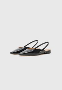 Black patent leather slingback shoes with a pointed toe, open sides, and flat heel; features minimal hardware detail.