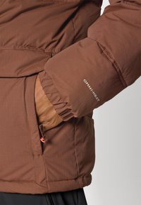 Braune isolierte Jacke mit strukturiertem Finish, featuring elastische Bündchen, Seitentasche mit Reißverschluss und "OMNI-HEAT"-Logo auf dem Ärmel.