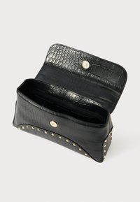 Crna clutch torbica s teksturom krokodila sa zlatnim čavlima duž rubova, otvoreni preklop s magnetskim zatvaranjem, prikazuje prazan unutrašnjost.