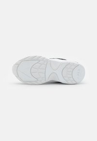 Bílá podešev tenisky s texturovanou gumou pro lepší přilnavost, s zaobleným tvarem a viditelnými vzory na podrážce. Logo na patě. Minimalistický design.