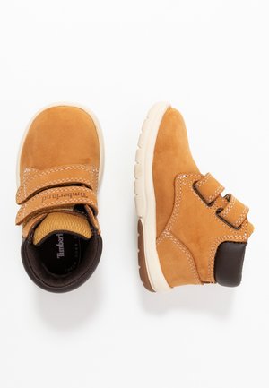 Botas de ante color tostado para niños pequeños, con cuello acolchado negro, doble tira de velcro y suelas de goma blancas, mostradas desde vistas superior y lateral.