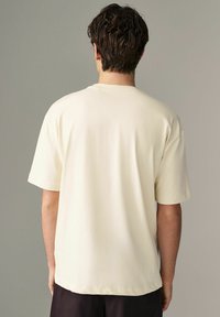 Kurze Ärmel, crèmefarbene T-Shirt aus weichem Stoff. Verfügt über einen runden Halsausschnitt und eine lockere Passform mit geradem Saum.