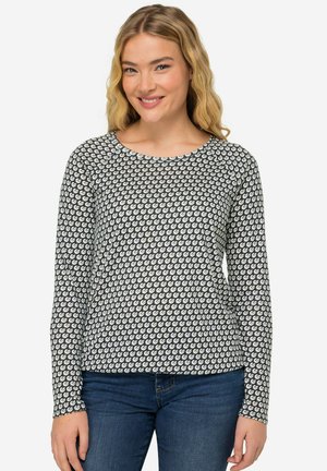 Top a maniche lunghe nero con un motivo circolare bianco, scollatura rotonda, tessuto morbido e design aderente, abbinato a jeans blu scuro.