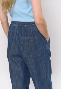 Pantaloni din denim cu croială lejeră, talie elastică și buzunar vizibil în spate. Culoare albastru închis cu un model subtil de textură.
