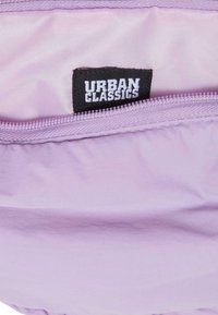 Bolsa lila con una superficie texturizada, que cuenta con una cremallera y una etiqueta interior marcada "URBAN CLASSICS" en blanco y negro.