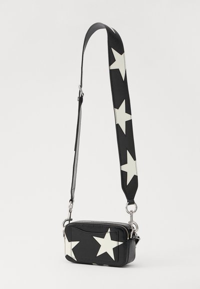 Crni crossbody torba s velikim bijelim uzorcima zvijezda, s patentnim zatvaračem i odvojivim remenom koji kombinira teksture tkanine i kože.
