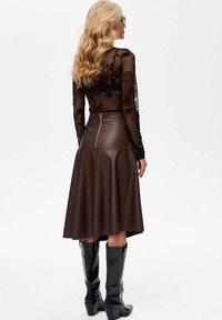 Zwarte doorzichtige blouse met lange mouwen en bloemborduursel. Bruine leren rok tot de knie met een ritssluiting aan de achterkant. Zwarte kniehoge laarzen.