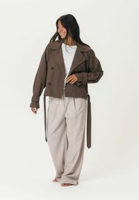 Pruun lühike trench coat suurte mustade nööpidega, laia kraega ja lipsuluku, koos heleda beeži laia jalaga pükstega.