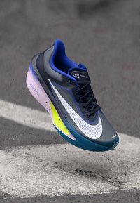 Zapatilla de running Nike Zoom Fly en gris, con un swoosh blanco, acentos azules y una suela degradada con detalles en rosa y amarillo.