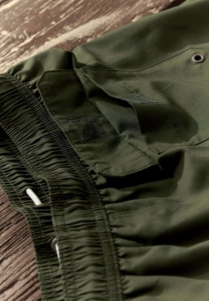 Krótkie spodenki w kolorze oliwkowej zieleni wykonane z gładkiej, lekkiej tkaniny, posiadają elastyczną talię, regulowany sznurek oraz kieszeń na rzep.