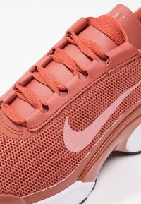Nike running shoe with a breathable coral mesh upper, smooth leather accents, and pink logo. Features flat coral laces and minimalistic design.