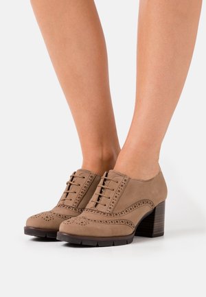 Taupe Wildleder Schnürschuhe mit Wingtip-Design, ausgestattet mit dekorativen Perforationen und einem Holzblockabsatz. Texturierte Oberfläche und robuste Sohle.