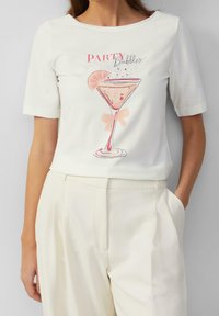 T-shirt blanc à manches courtes présentant un design de verre à cocktail imprimé avec des accents roses et le texte "PARTY bubbles". Texture en coton lisse.