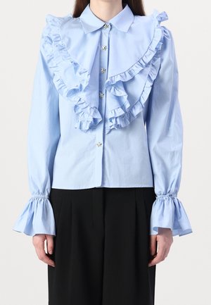 Jasnoniebieska bawełniana bluzka z dużym falbaniastym kołnierzem, guzikami w kształcie gwiazdek oraz falbaniastymi mankietami. Dopasowany krój z długimi rękawami.