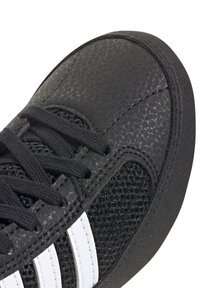 Svarta sportskor med en texturerad ovandel, som har nätpaneler, svarta snörningar och tre vita ränder. Rund tå och dämpad sula.