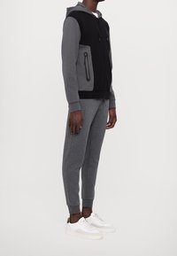 Svart och grå zip-up hoodie med huva, med zip-fickor. Matchar med grå joggare och vita sneakers. Enkel textur och avslappnad passform.