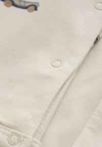 Bodysuit en coton pour bébé de couleur crème, arborant des motifs de voitures bleu clair. Fermeture par pressions blanches sur le bas. Texture douce.